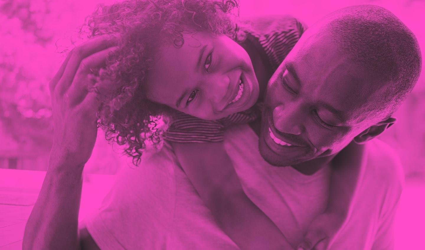 A man smiling while hugging a young child who is also smiling